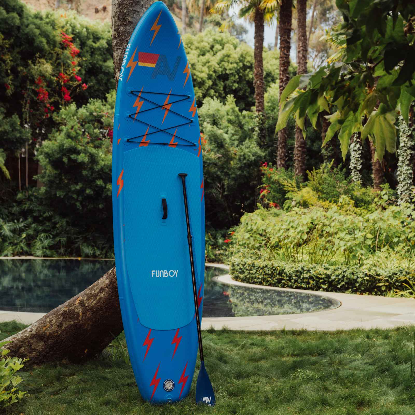 Blue paddleboard with red lightning bolt designs on a grassy area with greenery in the background