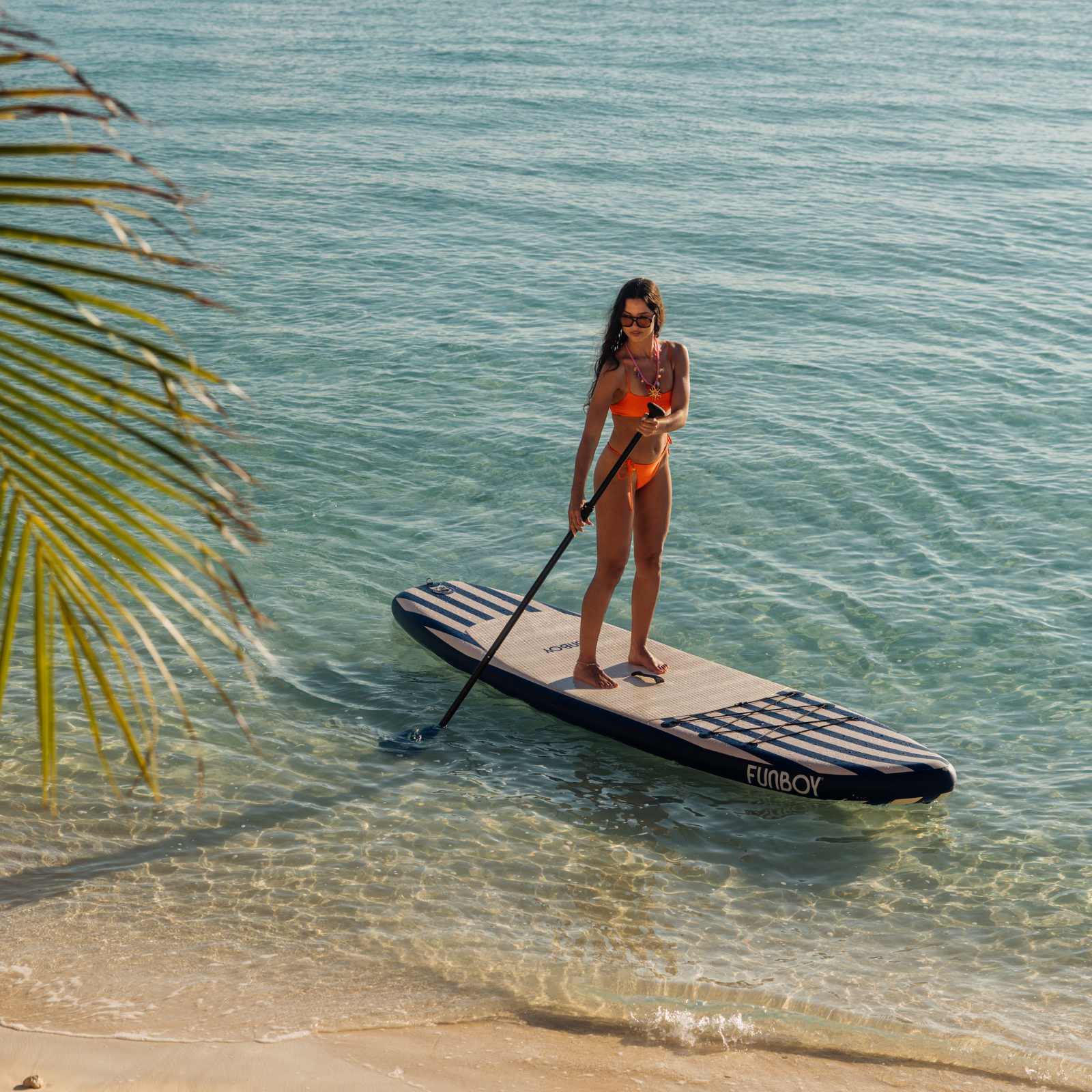Woman paddleboarding on a clear blue ocean with a palm tree in the background