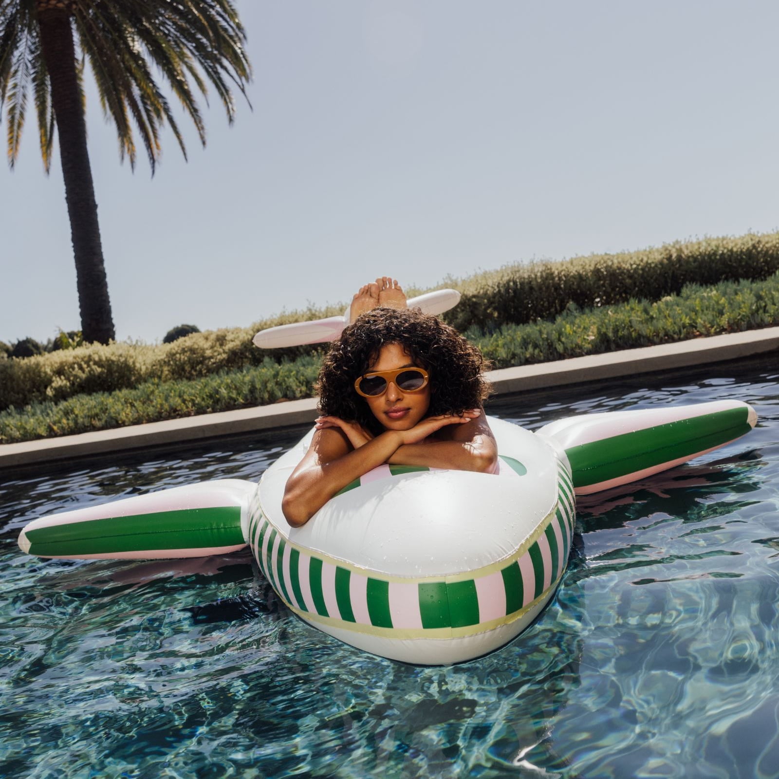 Woman lounging on a striped pool float in a pool with palm trees in the background