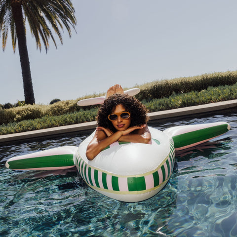 Woman lounging on a striped pool float in a pool with palm trees in the background