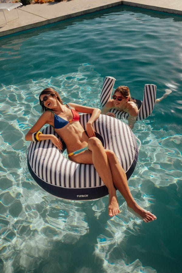 Two women lounging on striped inflatable rings in a pool