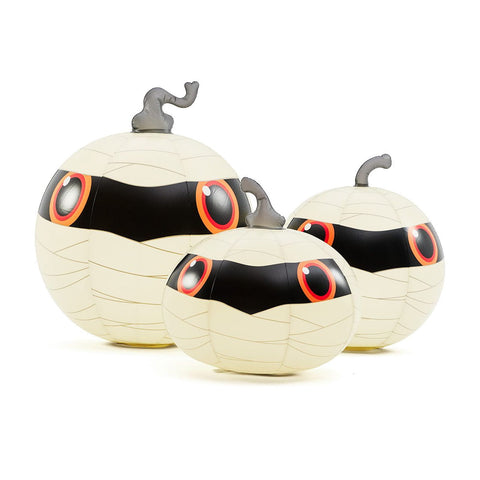 Three mummy-themed decorative pumpkins with cream-colored bodies wrapped in faux bandages, black facial masks, large red and black eyes, and small gray stems, shown on a white background.