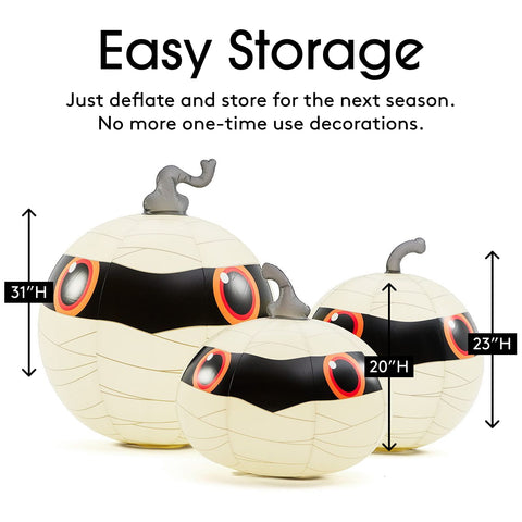 Three inflatable mummy-themed pumpkins shown on a white background with text reading 'Easy Storage' and height labels 31"H, 20"H, and 23"H. The pumpkins are cream with black mummy banding, orange eye details, and gray stems.