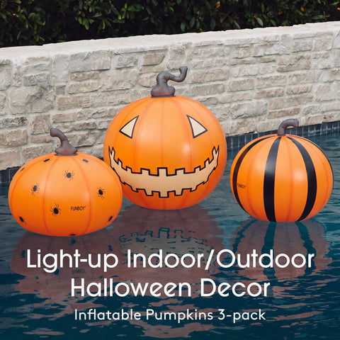 Three inflatable Halloween pumpkins in orange tones floating in a swimming pool. The center pumpkin has a carved jack-o'-lantern face, the left pumpkin has black spider details, and the right pumpkin has black vertical stripes.