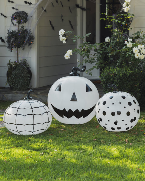 Three decorative pumpkins with black patterns on a grassy lawn