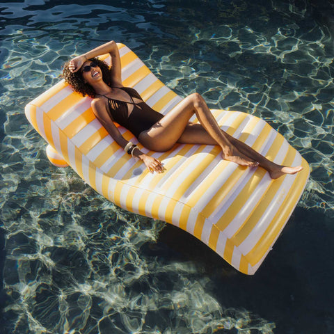 Woman lounging on a yellow and white striped pool float in clear water