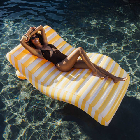 Woman lounging on a yellow and white striped pool float in clear water