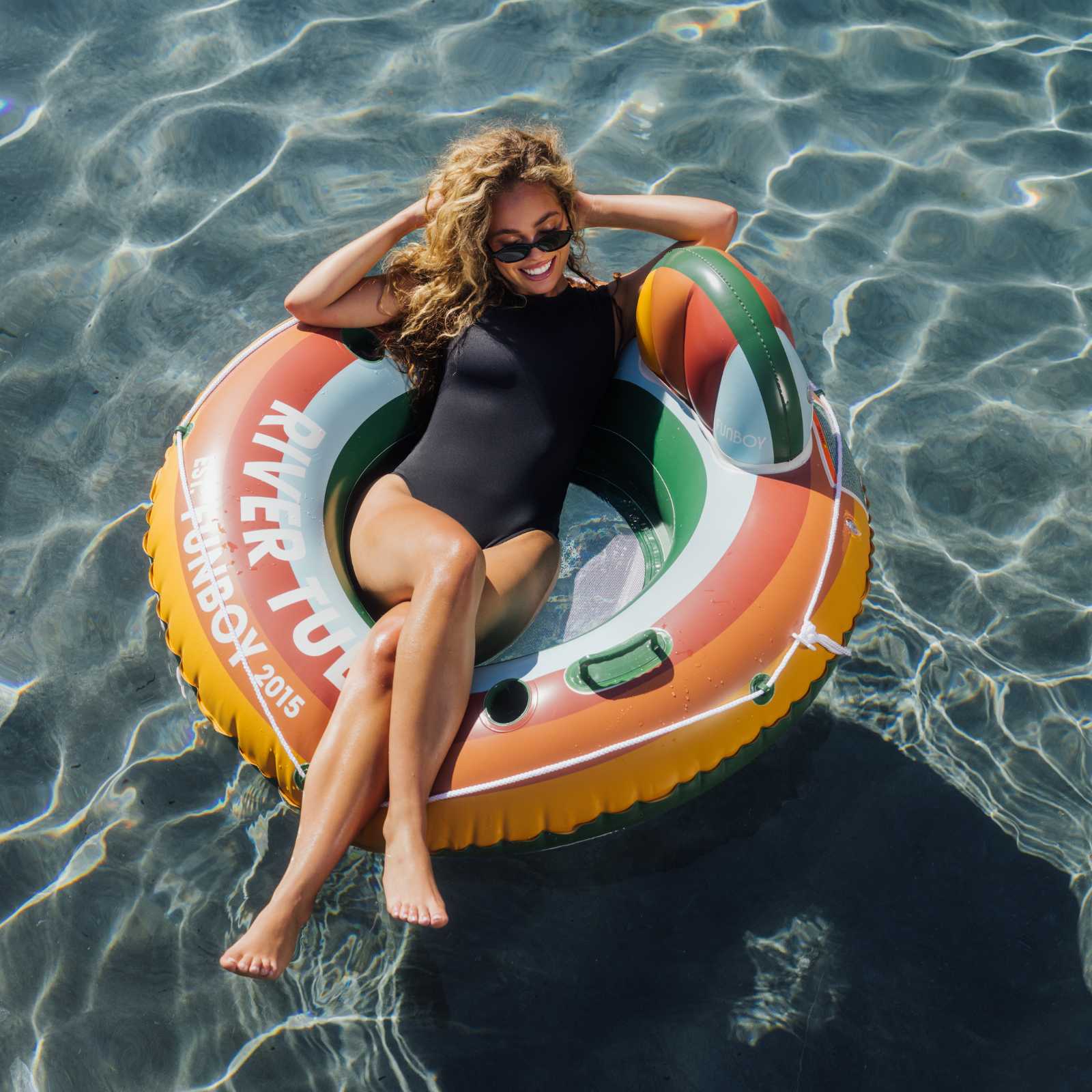 Woman in a black swimsuit sitting on a colorful inflatable ring in clear water.