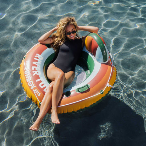 Woman in a black swimsuit sitting on a colorful inflatable ring in clear water.