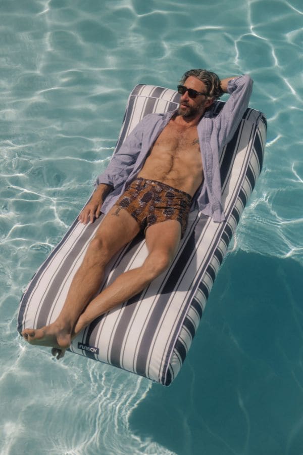 Man lounging on a striped inflatable navy stripe fabric pool float raft in clear blue water