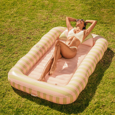 Woman lounging on a striped inflatable pool raft in a grassy area