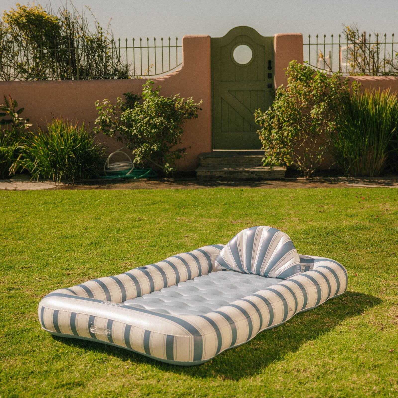 Inflatable striped pool float on grass with garden and wall in the background