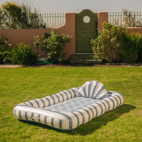 Inflatable striped pool float on grass with garden and wall in the background
