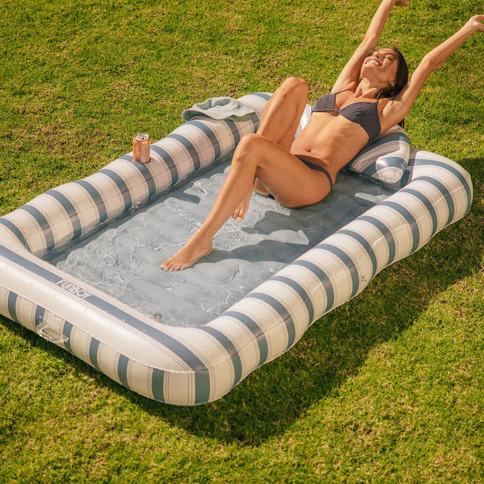 Woman relaxing on a striped inflatable tanning pool
 in a grassy area