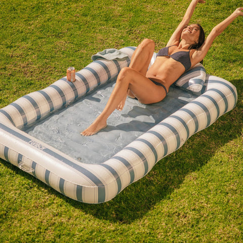 Woman relaxing on a striped inflatable tanning pool
 in a grassy area