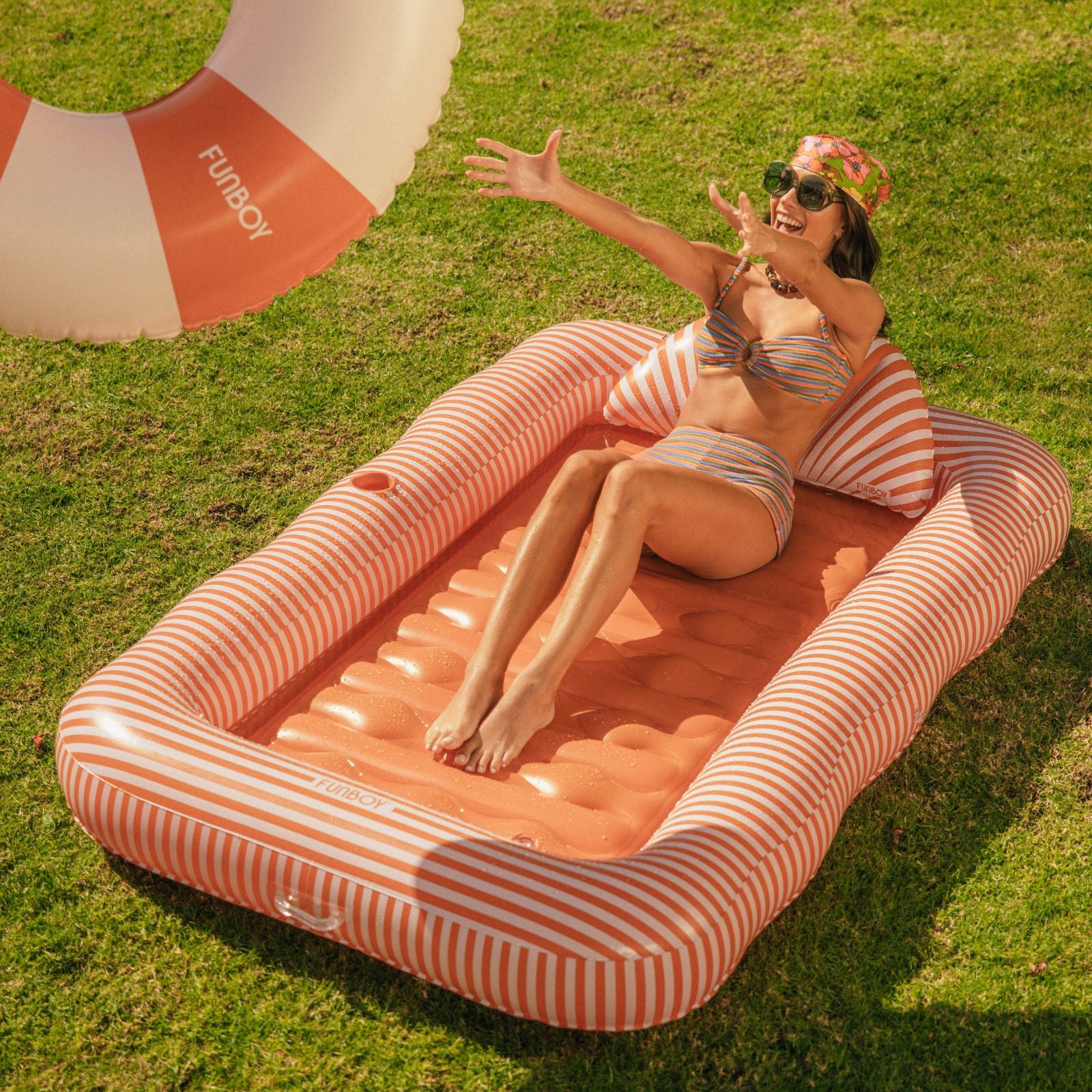 Woman lounging on a striped inflatable pool raft in a grassy area