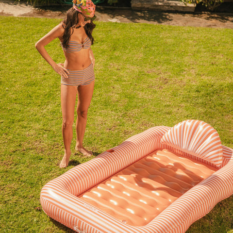 Woman in striped bikini standing next to an inflatable pool with shell design on grass