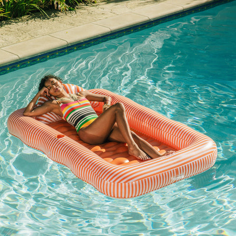 Woman lounging on a striped inflatable pool float in a swimming pool