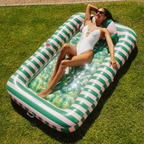 Woman lying on a green and white striped inflatable pool toy on grass
