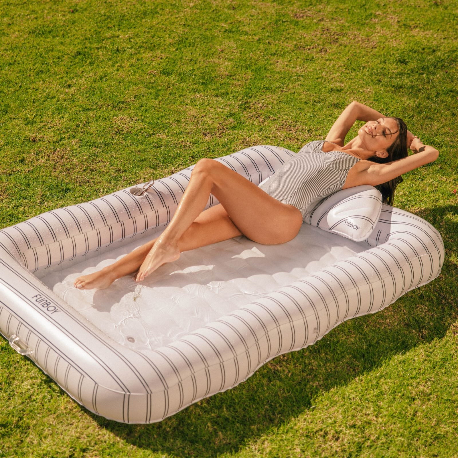 Woman lying on a striped inflatable pool raft in a grassy area