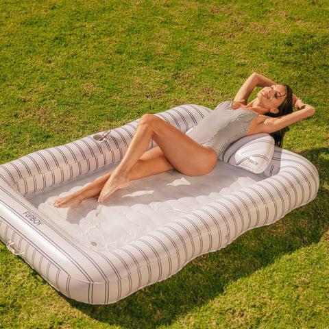 Woman lying on a striped inflatable pool raft in a grassy area