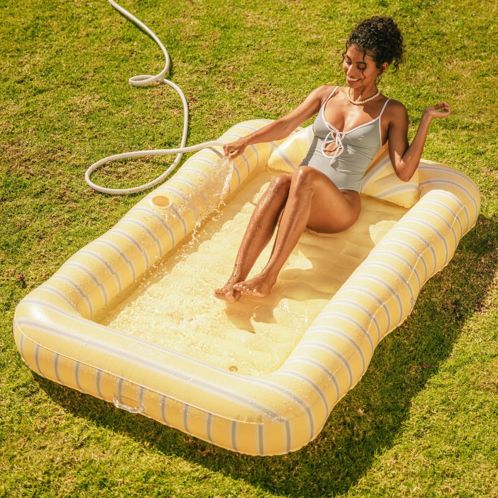 Woman sitting on a striped inflatable pool in a grassy area