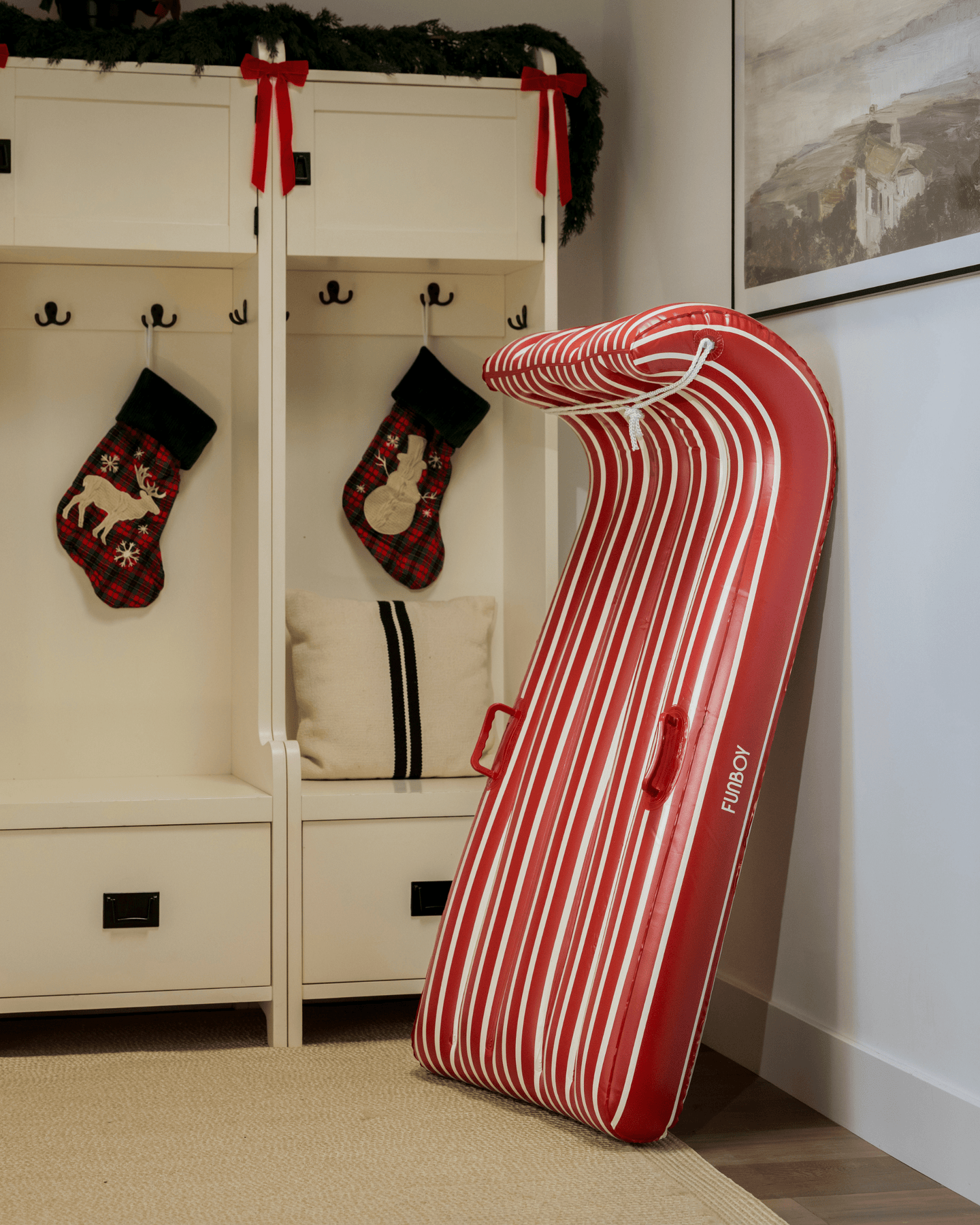 Red and white striped snow sled leaning against a white wall with Christmas stockings hanging on hooks.