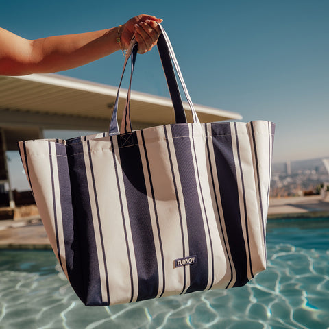 Striped tote bag held by a person by a pool with a clear blue sky.
