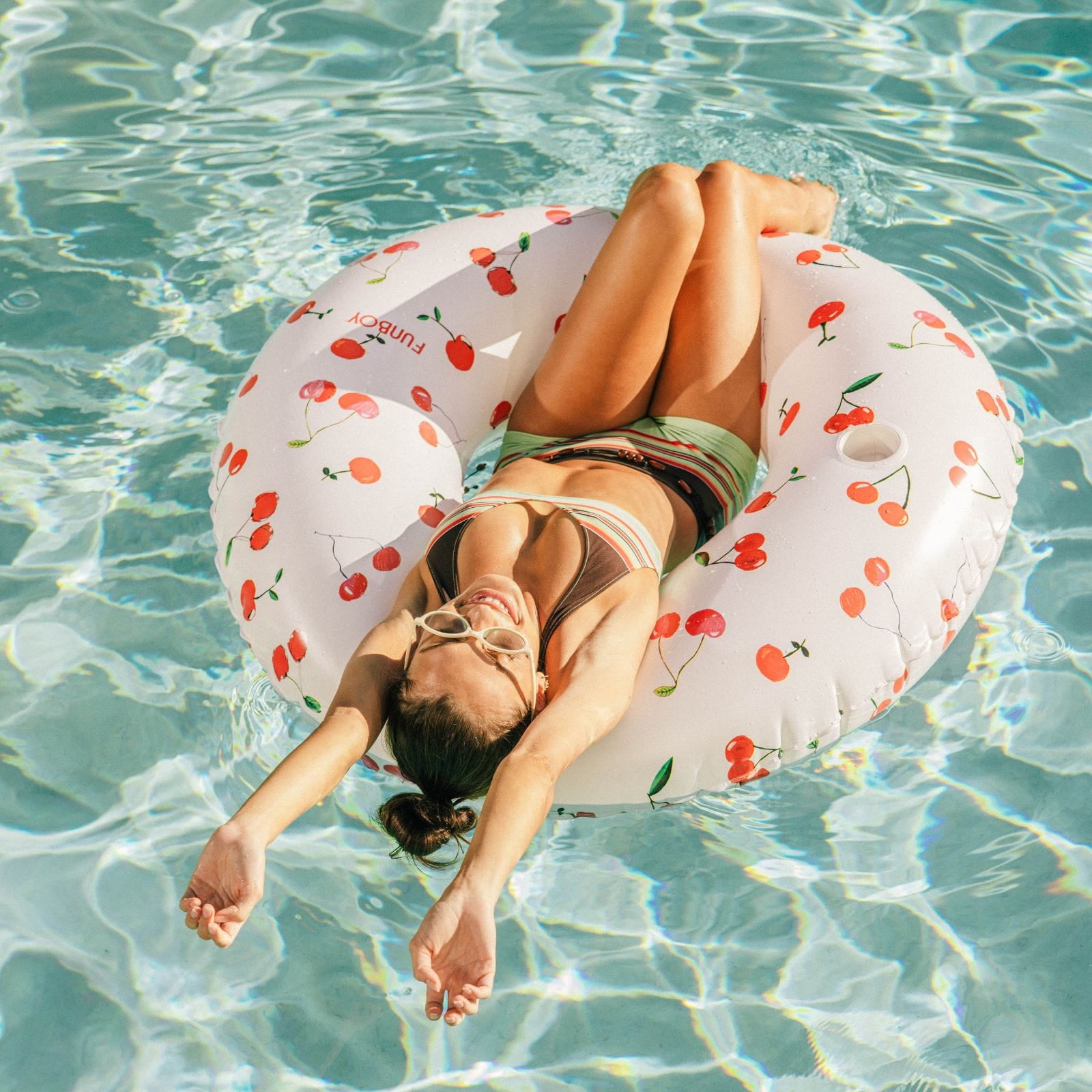 Woman relaxing on a cherry-patterned inflatable ring in clear pool water