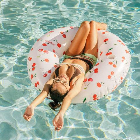 Woman relaxing on a cherry-patterned inflatable ring in clear pool water