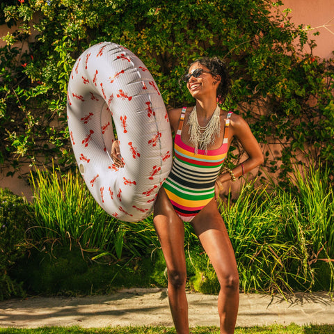 Woman in a colorful swimsuit holding a large inflatable ring with a garden background