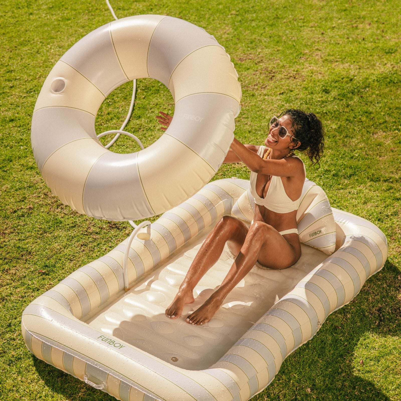 Woman sitting on a striped inflatable pool float with a life ring nearby on grass.