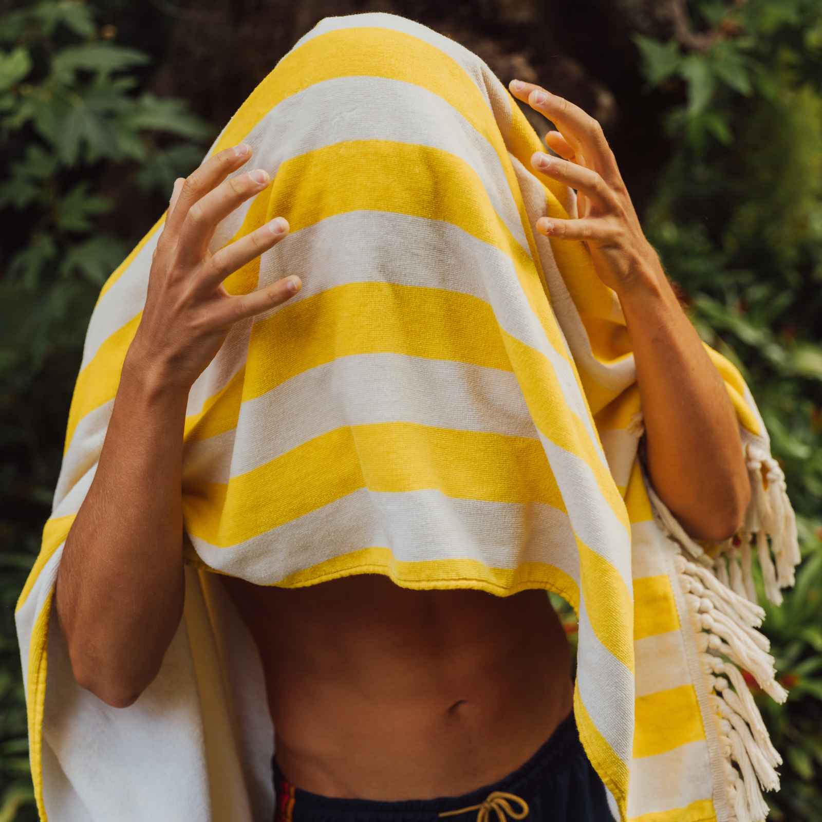 Person wrapped in a yellow and white striped towel with greenery in the background