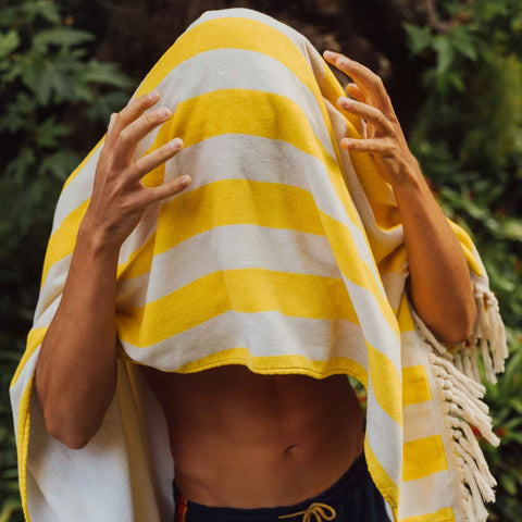 Person wrapped in a yellow and white striped towel with greenery in the background