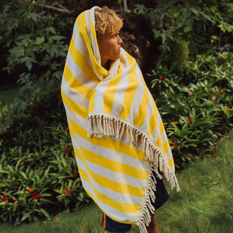Person wrapped in a yellow and white striped towel with fringes, standing outdoors.