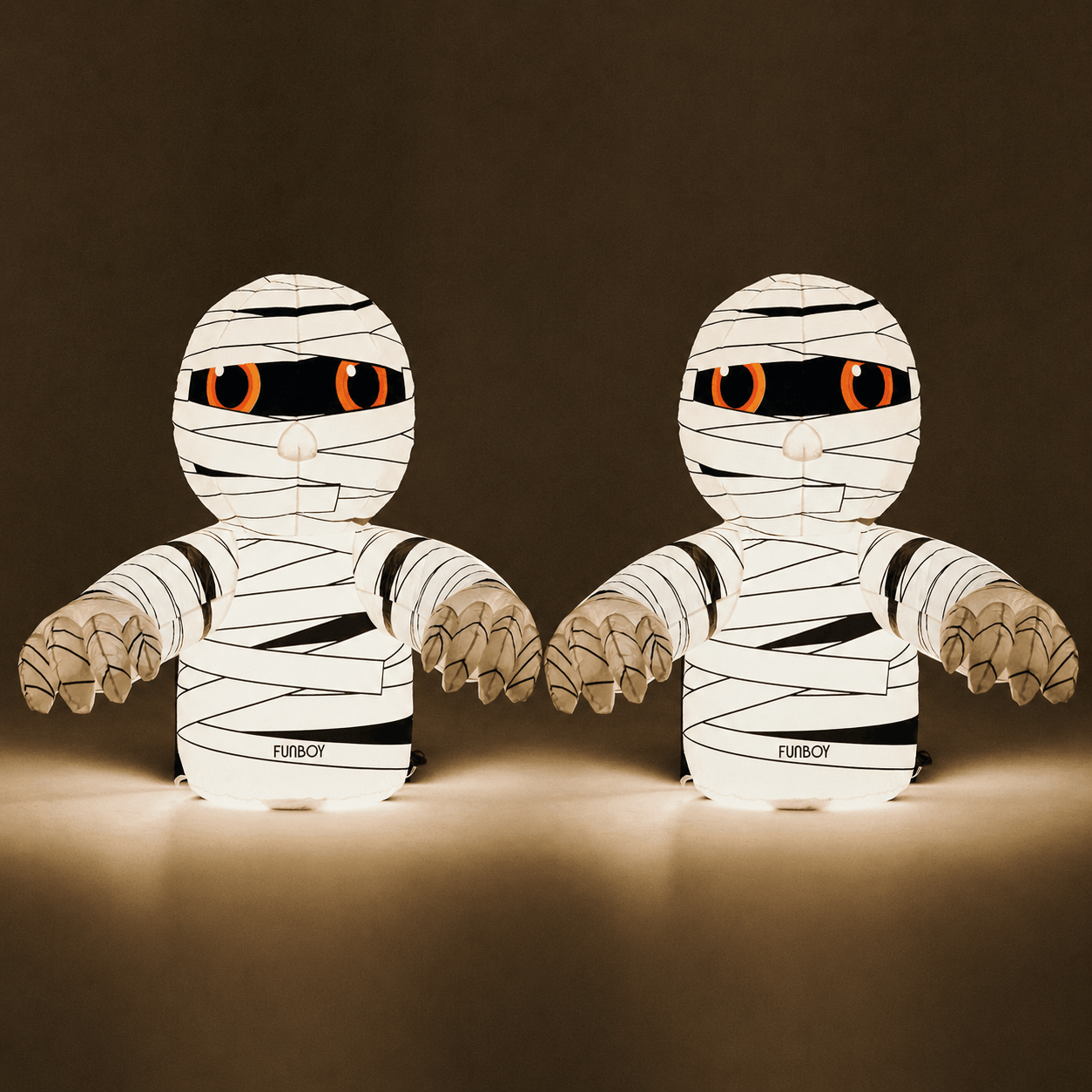 Two mummy-shaped decorative figures with glowing orange eyes and black printed text near the base, shown against a dark brown background.