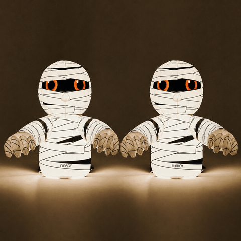 Two mummy-shaped decorative figures with glowing orange eyes and black printed text near the base, shown against a dark brown background.
