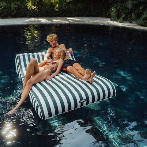Two people relaxing on a striped pool float in a pool. XL Green Fabric Lounger