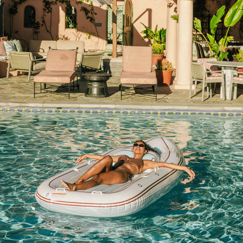 Woman relaxing on an inflatable yacht pool float in a pool with a sunlit patio in the background