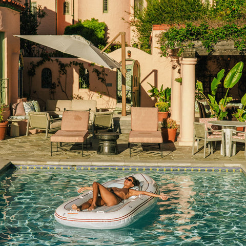Woman relaxing on a yacht pool float in a luxurious outdoor setting with a pool and lounge chairs.