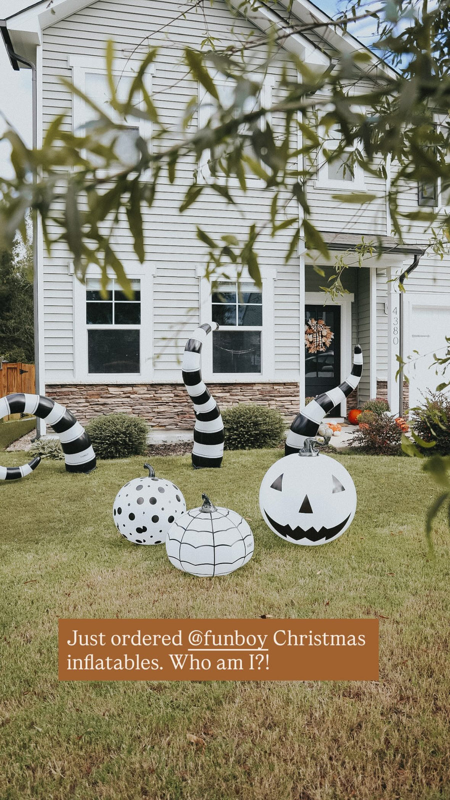 Black and white Halloween yard decorations displayed on a green lawn in front of a white house, including spiderwebs, striped spider legs, and jack-o'-lantern pumpkins. A text overlay at the bottom reads, 'Just ordered @funboy Christmas inflatables.